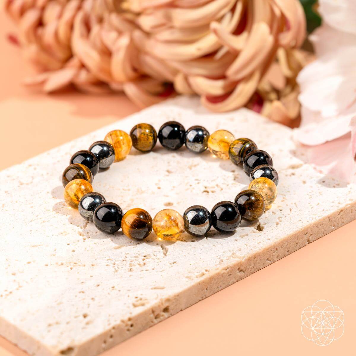 The Sacred Healing & Protection Trio by Conscious Items—a Black Friday exclusive bracelet with black, silver, and amber-yellow beads—is shown on a stone slab with soft-focus flowers in the background.