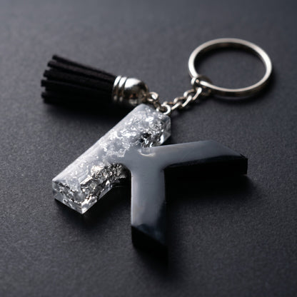 Resin keychain of the letter K with half silver leaf and half solid black, featuring a black tassel and silver ring.