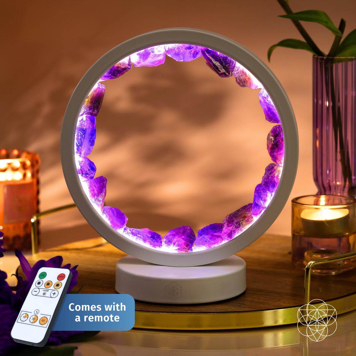 The Stress Less, Sleep More – Amethyst Healing Lamp by Conscious Items features a circular design with purple crystals, emits calming light for a healing atmosphere, and includes a remote control. Displayed on wood with candles and decor.