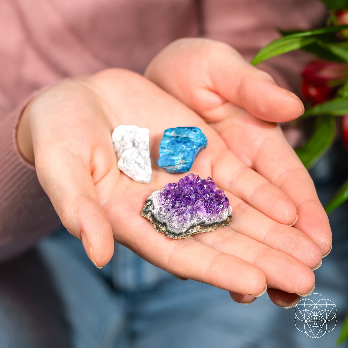 A person holds The Anti-Anxiety Trio by Conscious Items—white, vivid blue, and purple amethyst stones—in their hand. Green leaves, jeans, and a pink top add to the soothing scene with these calming crystals.