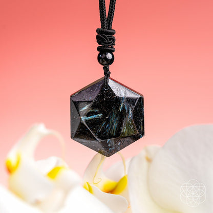 The Arfvedsonite Deep Healing Pendant by Conscious Items features a hexagonal black stone with blue-green streaks on a black cord, displayed with orchid petals—an ideal vision stone and crystal for emotional healing.