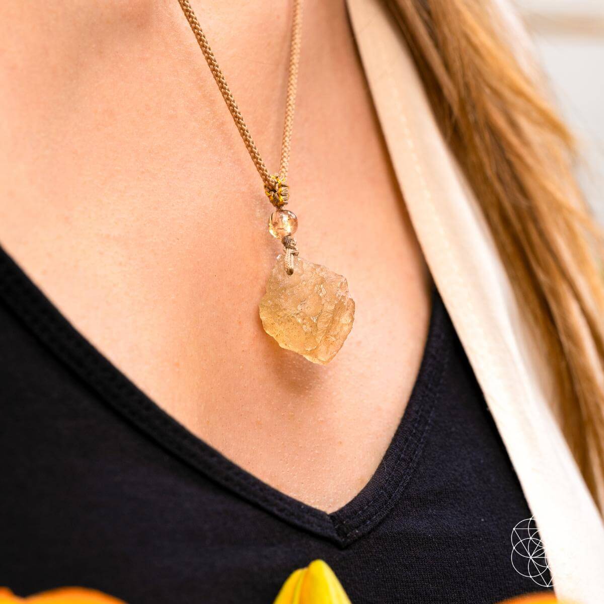 A close-up of a person wearing Conscious Items' The Destiny Relic – Libyan Desert Glass Pendant, a bold gold chain necklace, paired with a black top and cream outer garment.