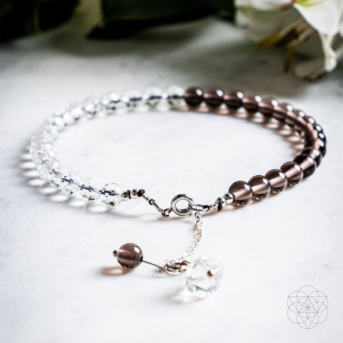 The Energy Shield Anklet by Conscious Items features clear and smoky brown beads in a gradient for chakra balance, finished with a silver clasp and dangling bead and crystal charm.