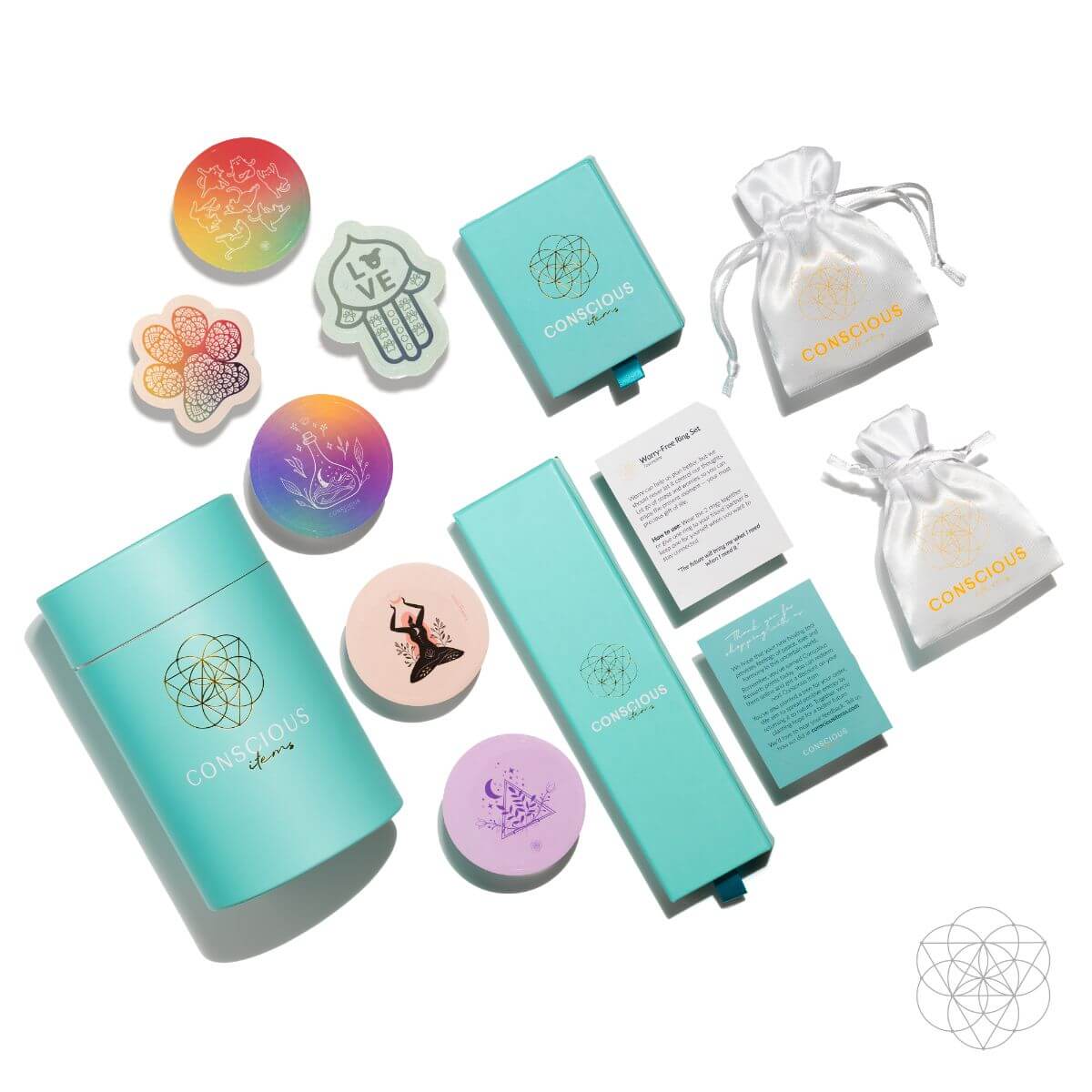 A flat lay features colorful round discs, teal Conscious Items packaging, info cards, and two white drawstring pouches with gold logos—highlighting The Prosperity Pendant by Conscious Items to attract wealth—all on a white background.