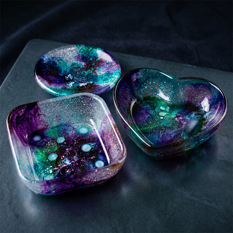 Three colorful resin dishes on a dark surface