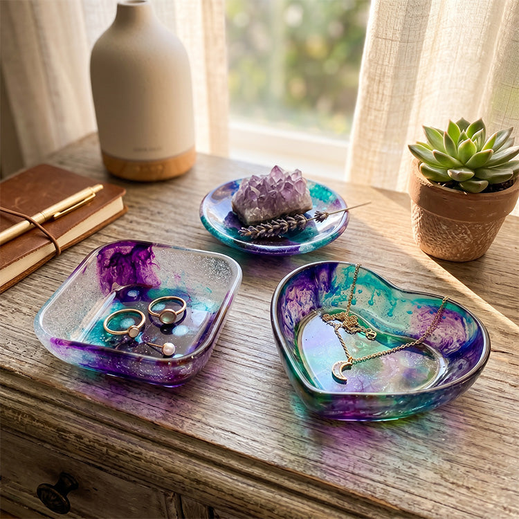 Three colorful jewelry dishes on a wooden surface with rings, necklaces, and crystals.